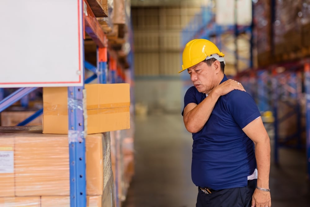 Man in warehouse holding shoulder in pain